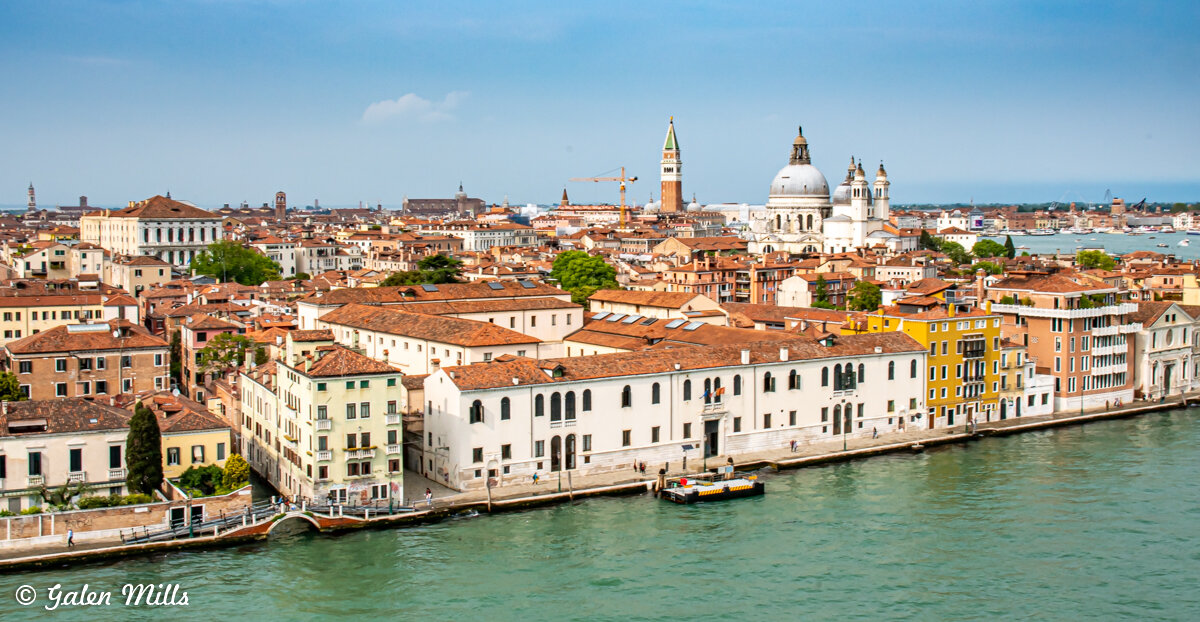 Aerial view of Venice, Italy with red-tiled rooftops, historic buildings, waterways, and the prominent dome of Santa Maria della Salute.
