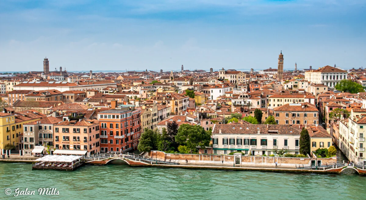 Aerial view of Venice, Italy, with red-roofed buildings, canals, and historic architecture under a blue sky.