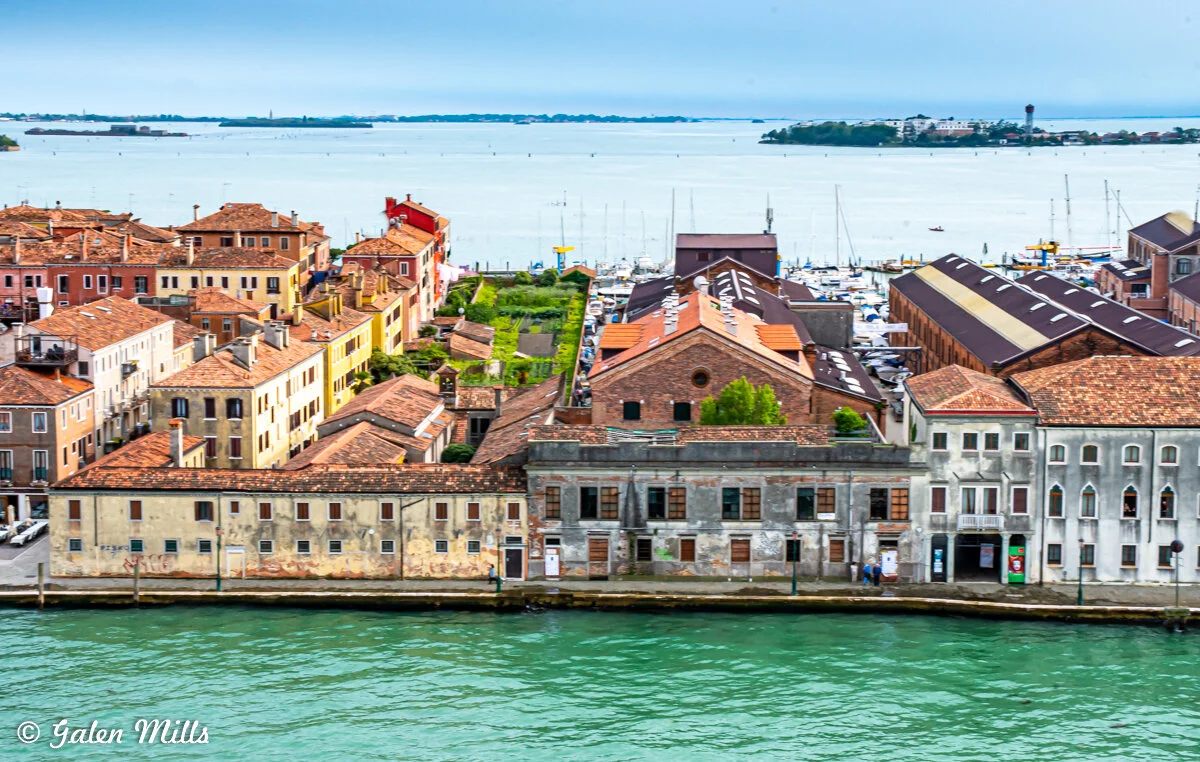 Aerial view of colorful buildings and canal in Venice, Italy with a marina and lagoon in the background.