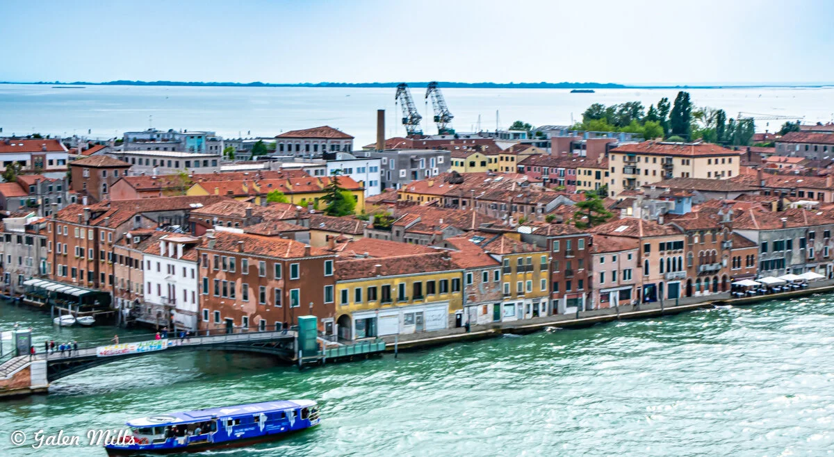 Aerial view of Venice, Italy with water canal, colorful historic buildings, and visible cranes in the background.