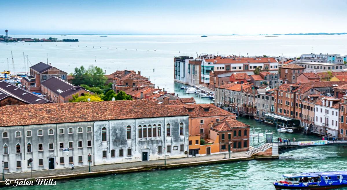 Aerial view of buildings and waterways in Venice, Italy, with red-tiled roofs and boats on the water.