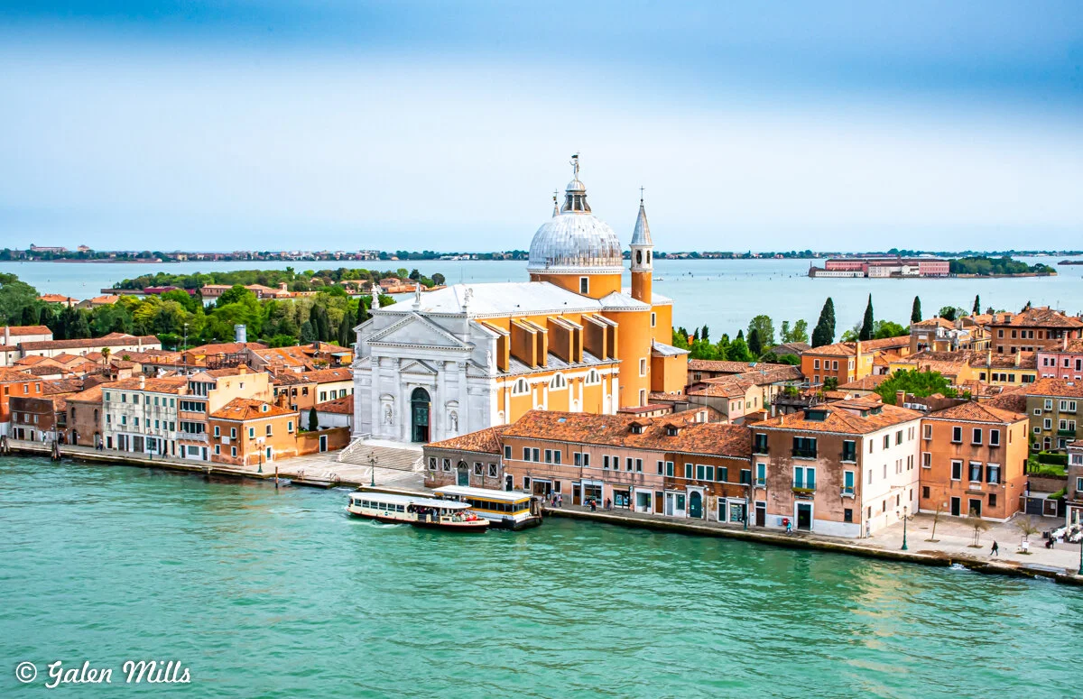 Aerial view of San Giorgio Maggiore, a church on the island of San Giorgio in Venice, Italy, surrounded by buildings, with the lagoon and more islands visible in the background.