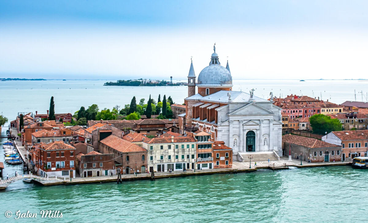 Aerial view of the Church of San Giorgio Maggiore, Venice, Italy, with its white facade, dome, and surrounding red-roofed buildings on a lagoon.