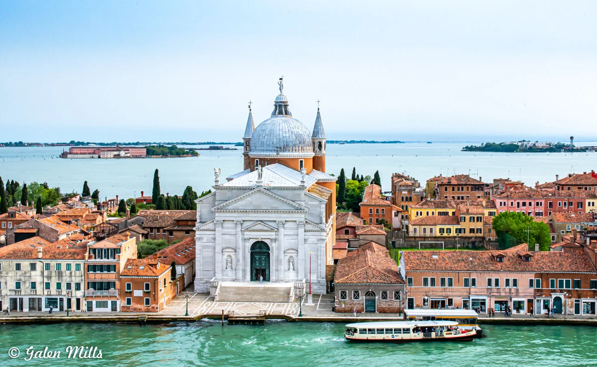 Scenic view of San Giorgio Maggiore island in Venice, Italy, featuring a white church with a dome, surrounded by traditional Venetian buildings and the lagoon.