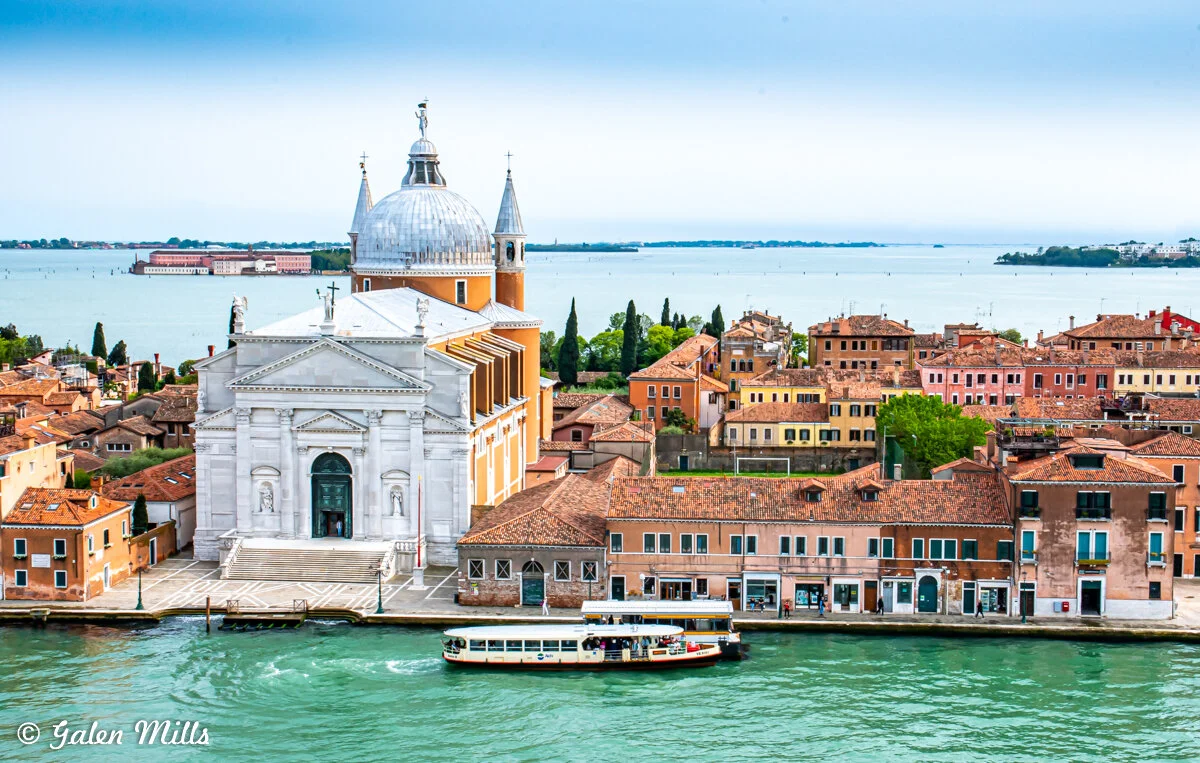 Venetian architecture with a white-domed church near a canal, boats on water, and colorful buildings in Venice, Italy.