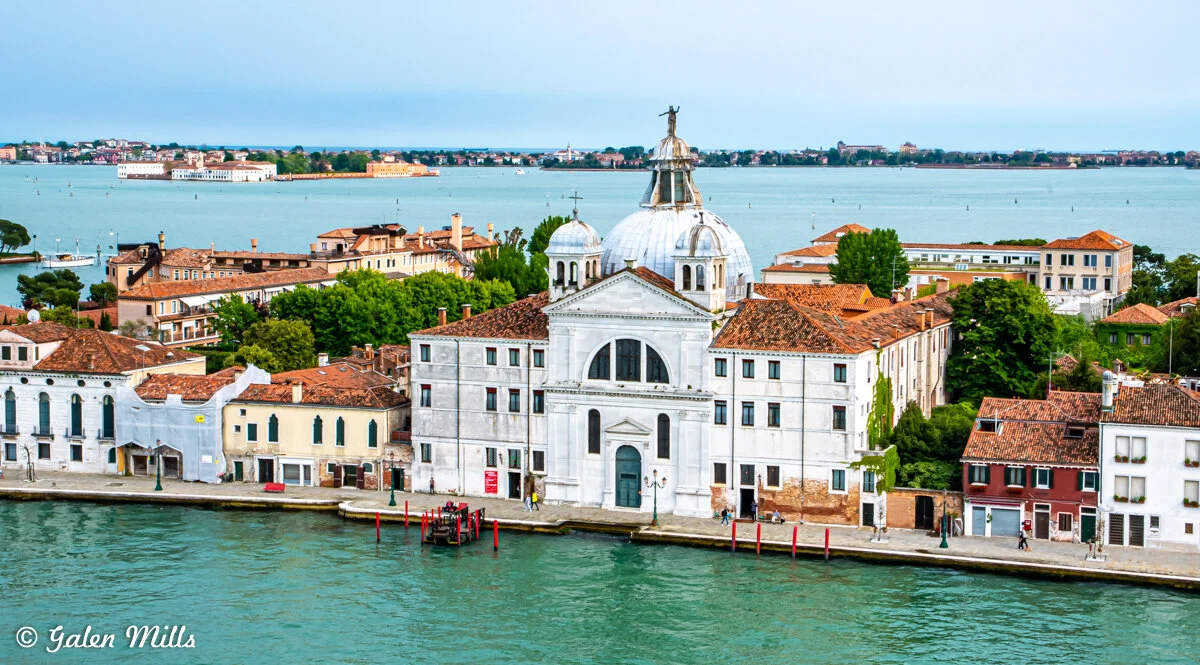 View of the Santissimo Redentore church and surrounding buildings on Giudecca Island, Venice, Italy, with water and distant islands in the background.
