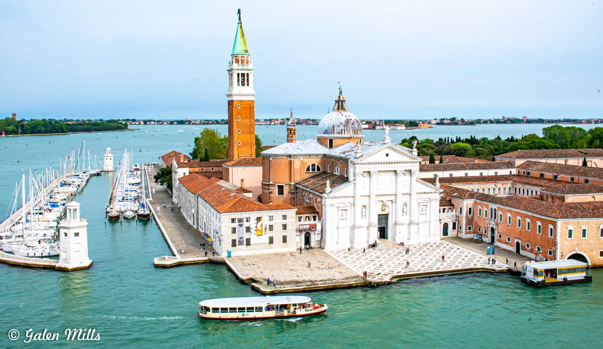 View of San Giorgio Maggiore Island in Venice, Italy, featuring the church with its iconic bell tower, surrounding buildings, moored yachts, and water traffic.