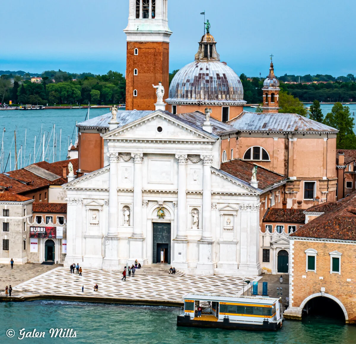 View of San Giorgio Maggiore church in Venice, Italy, with its white facade, dome, and bell tower, surrounded by water and buildings.