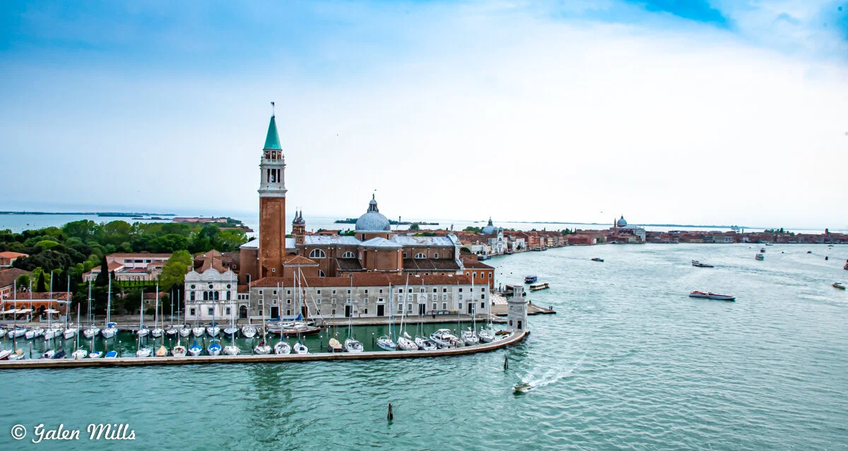 Aerial view of Venice, Italy, featuring San Giorgio Maggiore island with its prominent church and bell tower, surrounded by water and boats.
