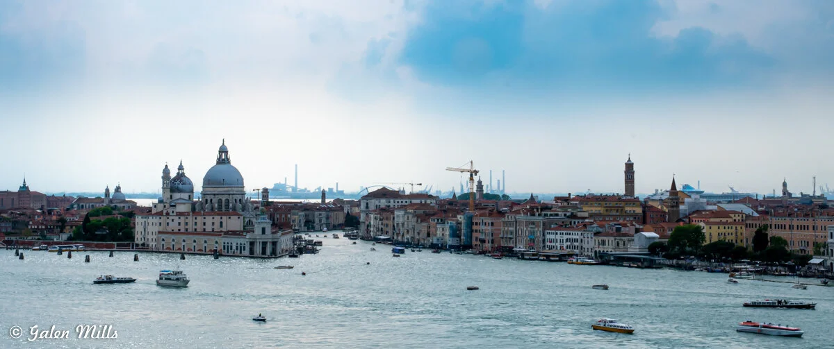 Panoramic view of Venice, Italy, featuring historic architecture, a domed basilica, and boats on the Grand Canal.