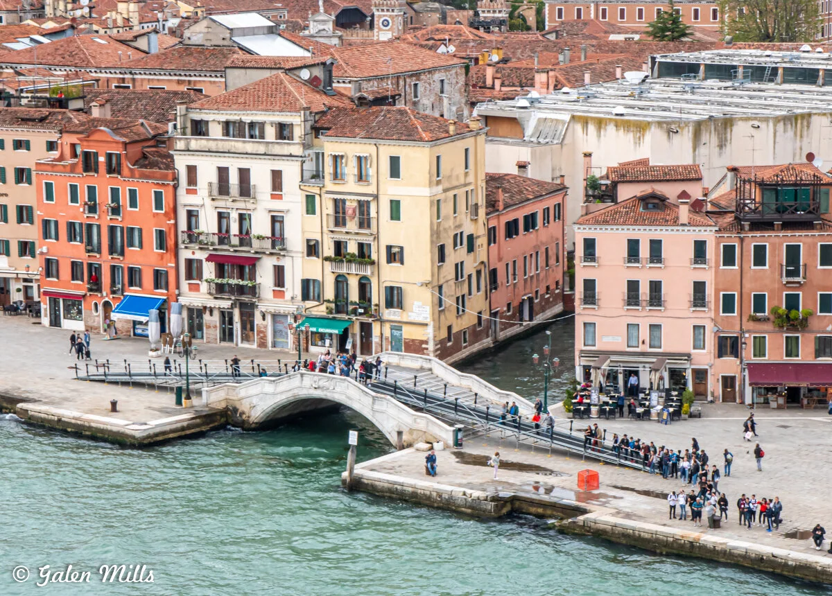 Venetian canal and bridge with people, colorful buildings, and waterfront in Venice, Italy.