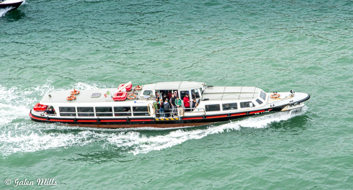 A canal ferry with passengers on a green waterway