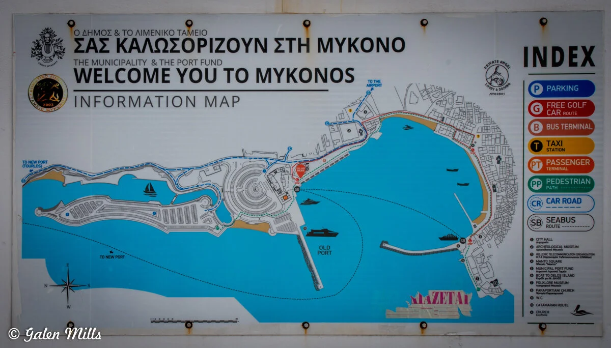 Mykonos information map with English and Greek text, showing town layout, port locations, and legend with symbols for parking, golf car routes, bus terminals, taxi stations, pedestrian paths, car roads, and seabus routes.
