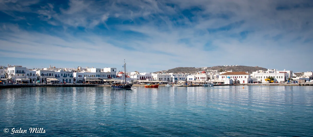 Scenic view of Mykonos harbor with traditional white buildings and boats docked at the waterfront.