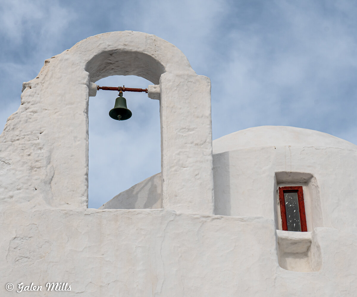 Whitewashed building with a bell and small window against a blue sky.