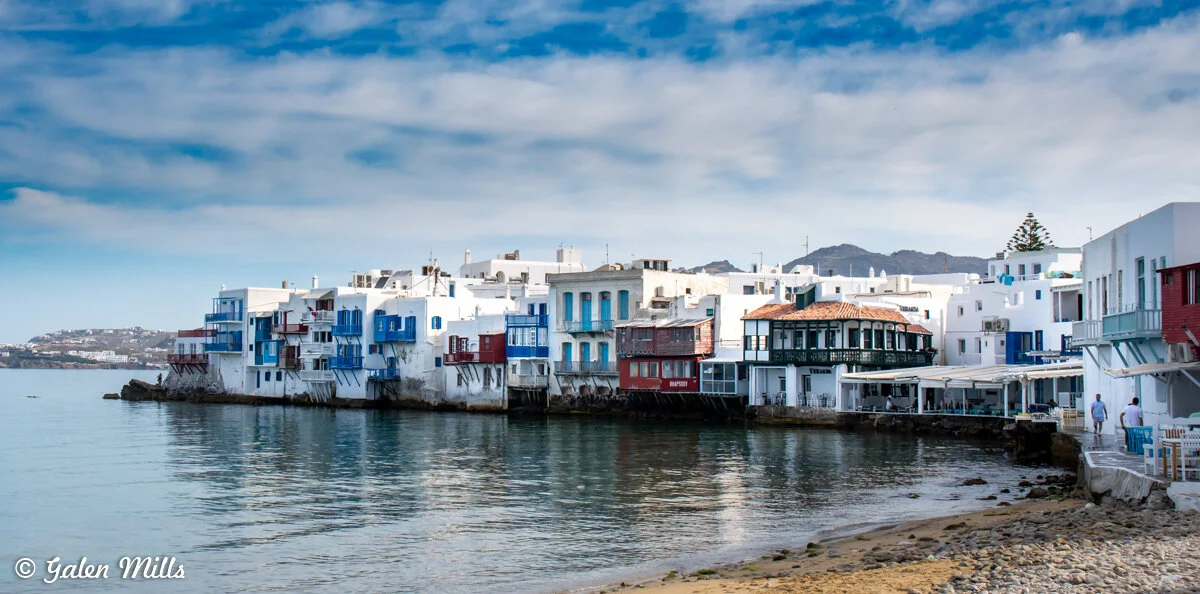 Scenic view of colorful buildings along the waterfront in Mykonos, Greece, with clear skies and calm water.