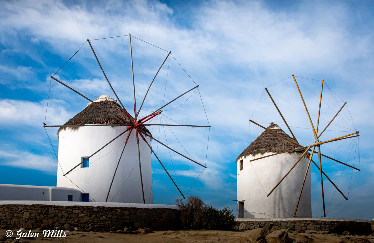 Traditional white windmills with thatched roofs against a blue sky in Mykonos, Greece.