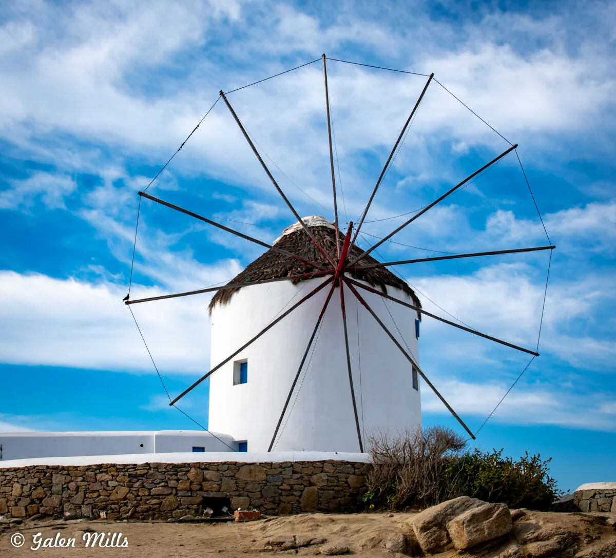 Traditional white Mediterranean windmill with wooden sails against a blue sky.