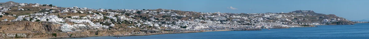 Panoramic view of a coastal town with white buildings on a hillside overlooking the ocean.
