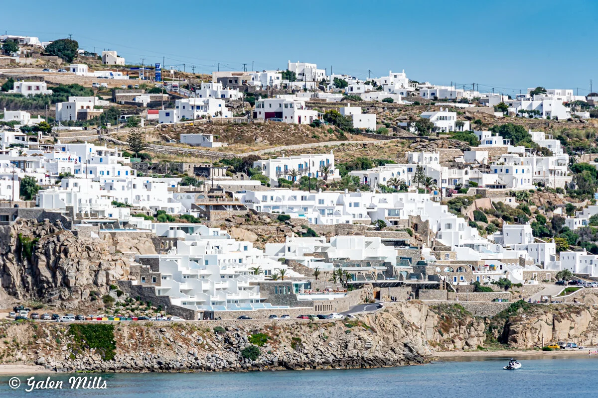 Panoramic view of Mykonos town with white buildings on a hillside, Greece, overlooking the sea.