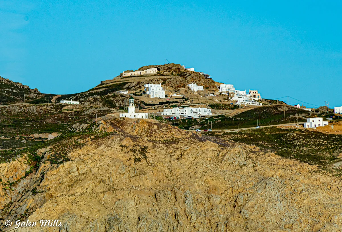 A rocky hillside with white buildings and a lighthouse, set against a clear blue sky.