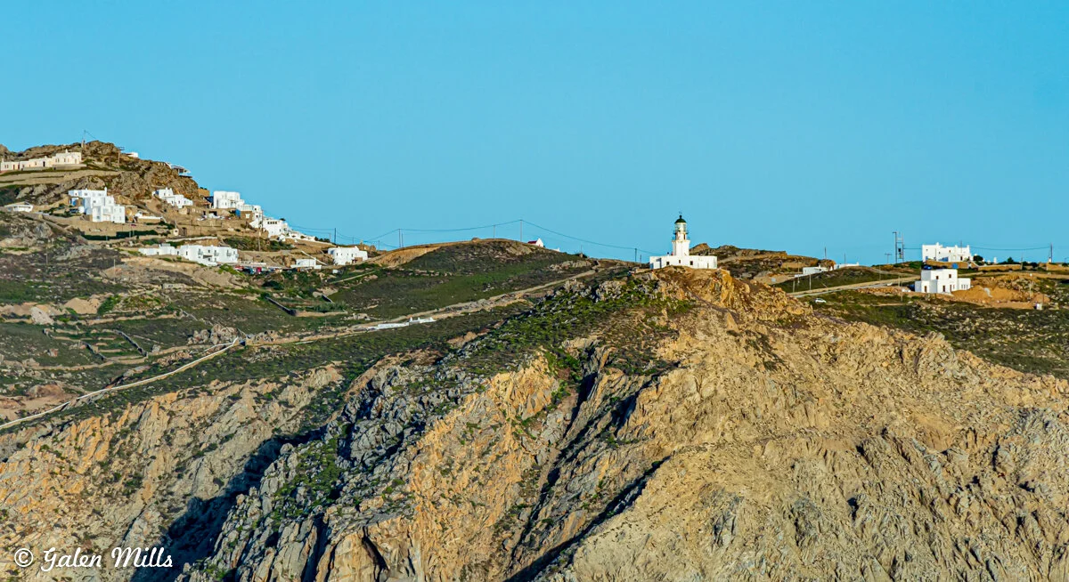 Hilltop view of white buildings and lighthouse on Serifos island, Greece, with blue sky.