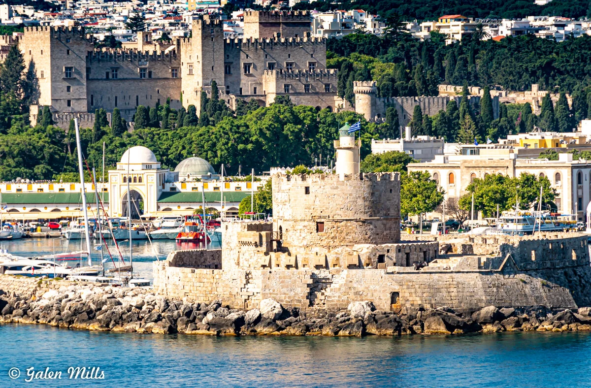 Medieval fortress and towers in Rhodes, Greece, with boats in the harbor.