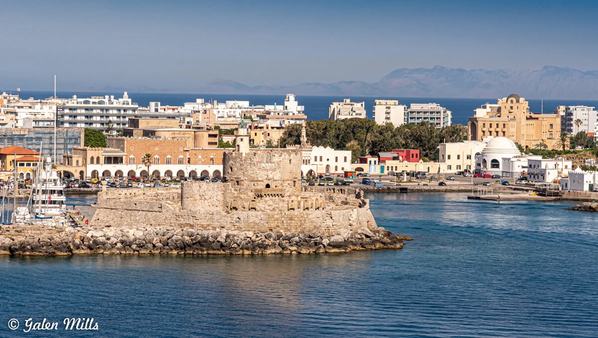 View of Mandraki Harbor with Fort Saint Nicholas and cityscape in Rhodes, Greece.