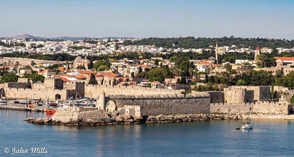 Panoramic view of Rhodes Old Town in Greece, with medieval stone walls, historic buildings, and a harbor with boats on a sunny day.
