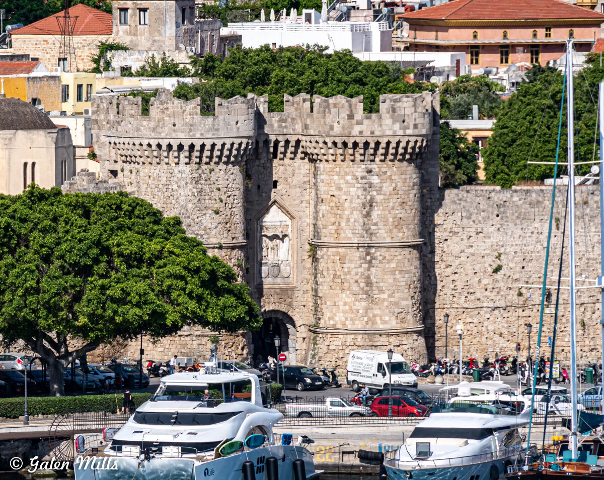 Historic stone gate and towers surrounded by greenery with boats in the foreground, showcasing a marina setting in a cityscape.