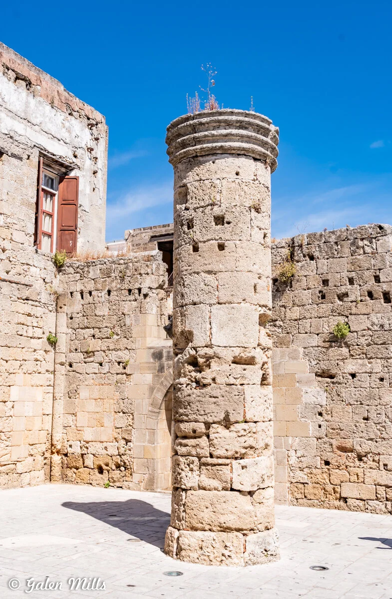 Ancient stone column in a historic courtyard with old stone walls and a blue sky background.
