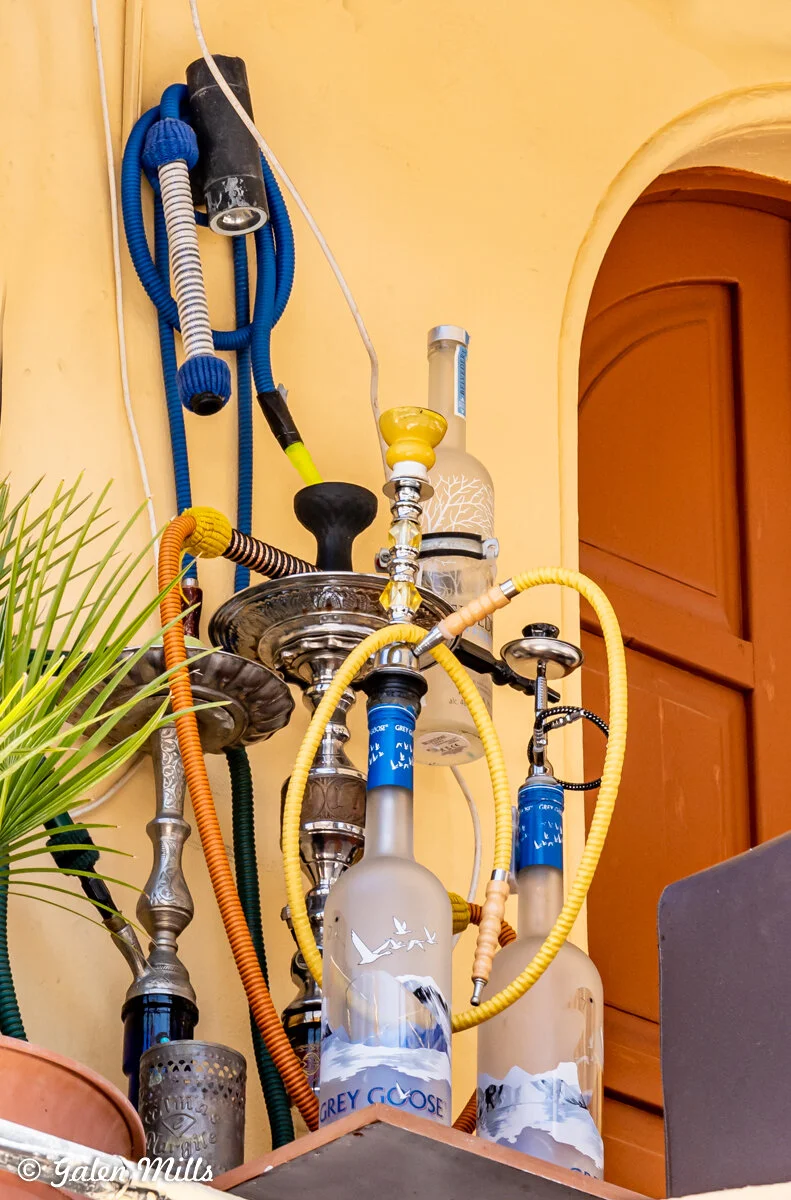 Hookahs with colorful hoses on a decorated shelf with Grey Goose vodka bottles, set against a yellow wall.