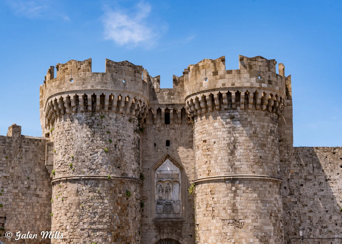 Medieval stone castle wall with two round towers and blue sky.