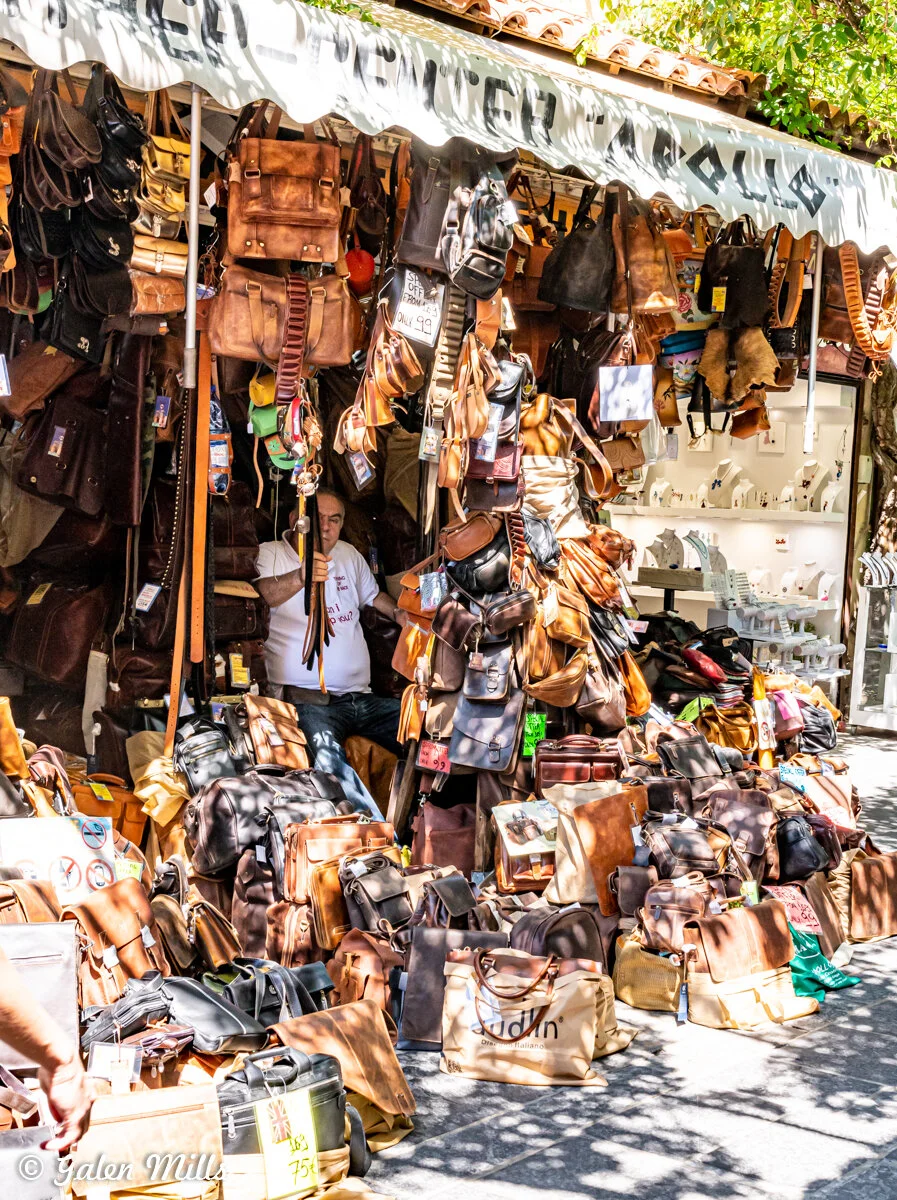 Outdoor market stall with leather bags and accessories displayed.