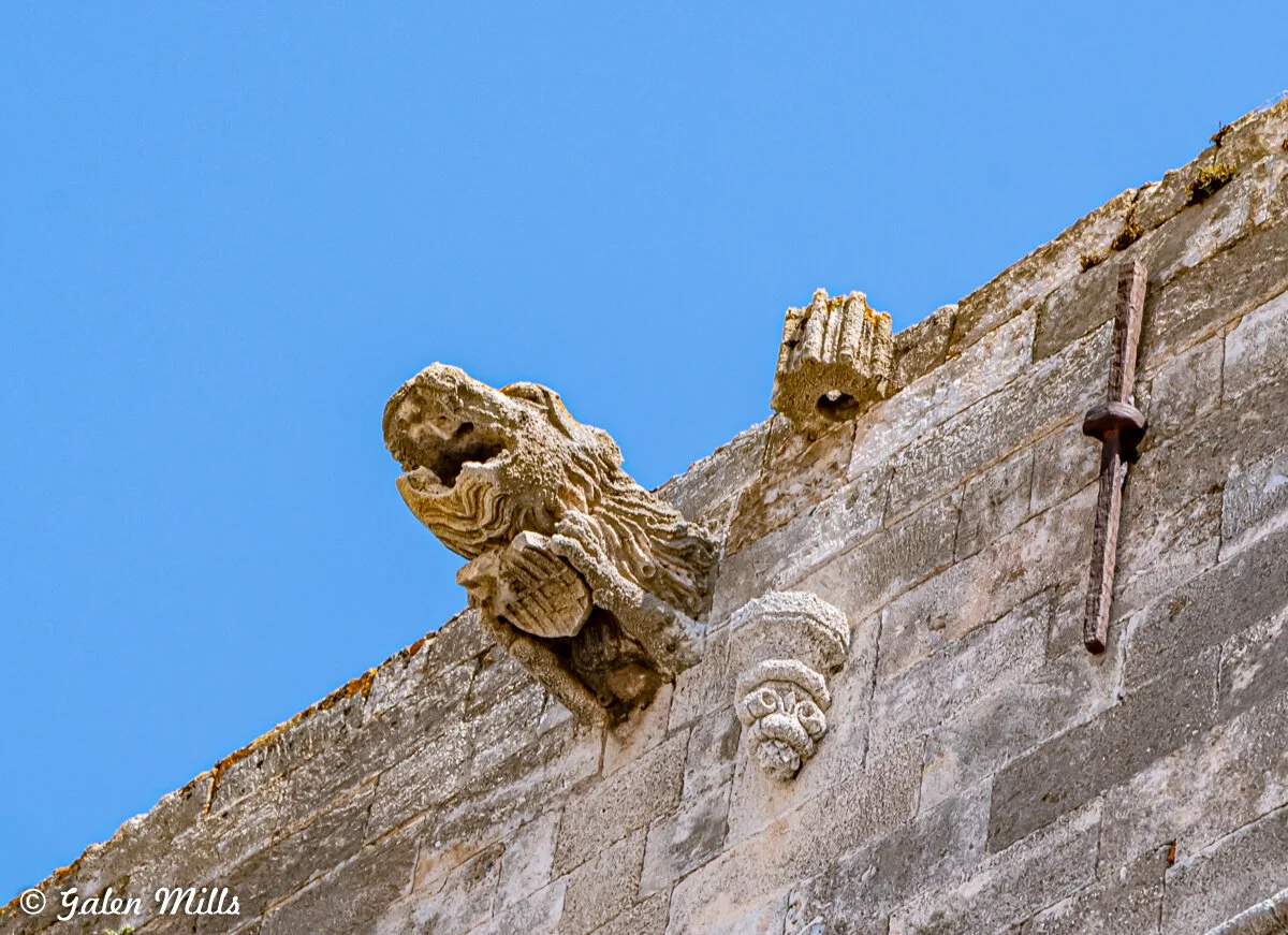 Stone gargoyle and architectural details on a historic building against a clear blue sky.