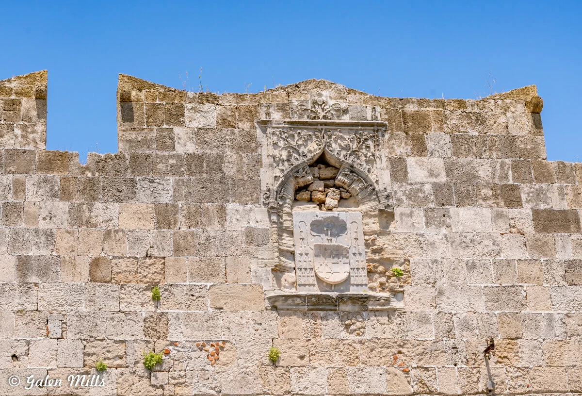 Stone wall with ornate carved arch and emblem on medieval fortress, clear blue sky background