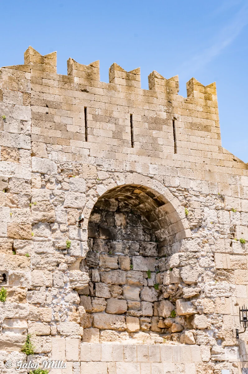 Ancient stone wall with an arched doorway and battlements under a clear blue sky.