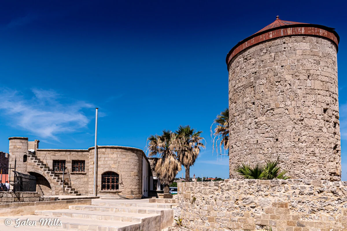 Historic stone tower and building with stairs, surrounded by palm trees and set against a clear blue sky.