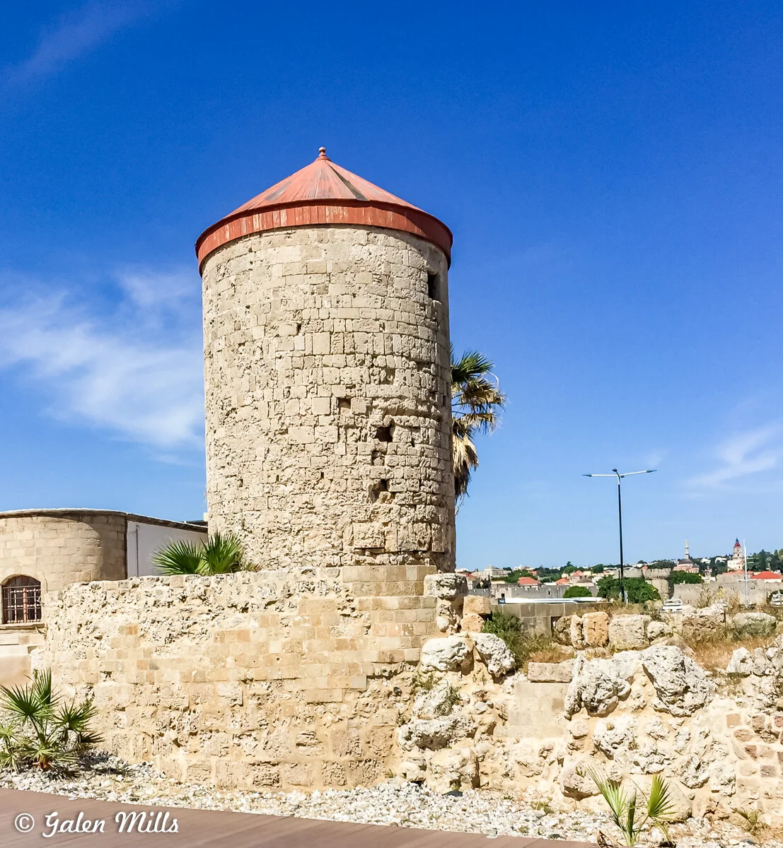 Historic stone tower with red roof in Rhodes, Greece, under clear blue sky.