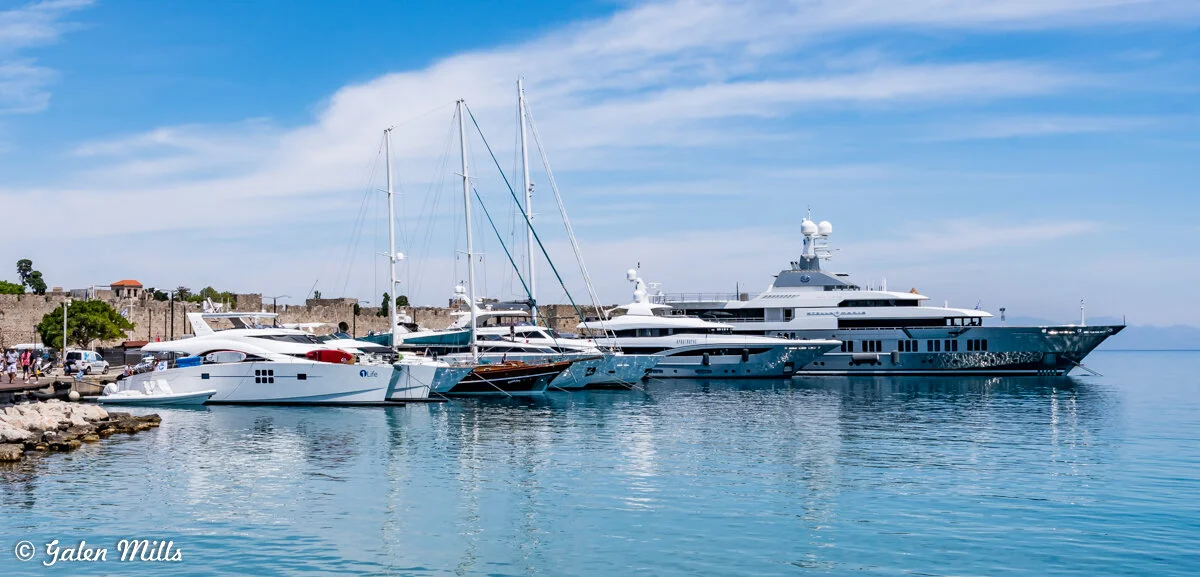 Yachts and sailboats docked at a marina with clear blue sky and calm water.