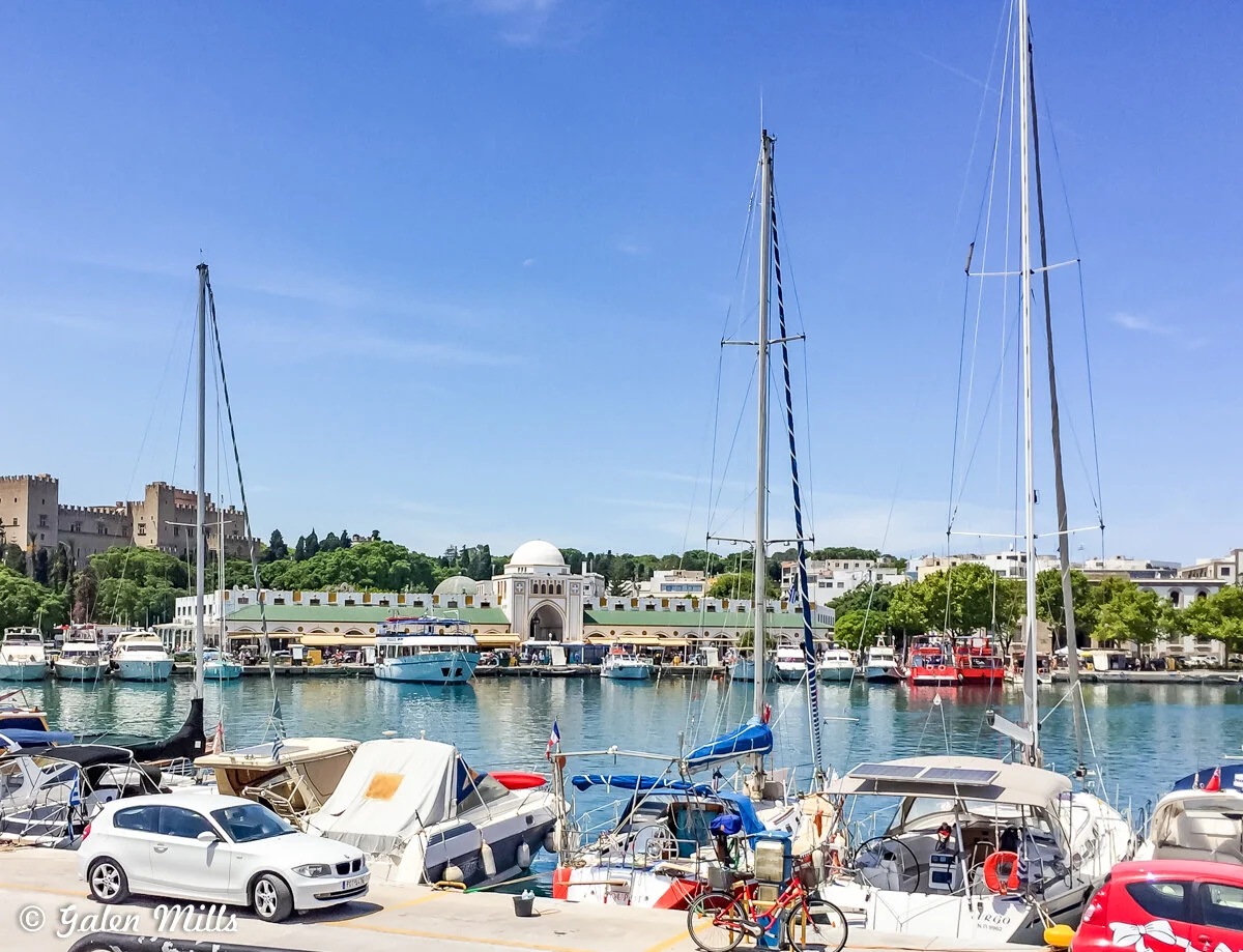 Scenic harbor view with boats and a waterfront town, featuring a domed building and a historic castle in the background, under a clear blue sky.