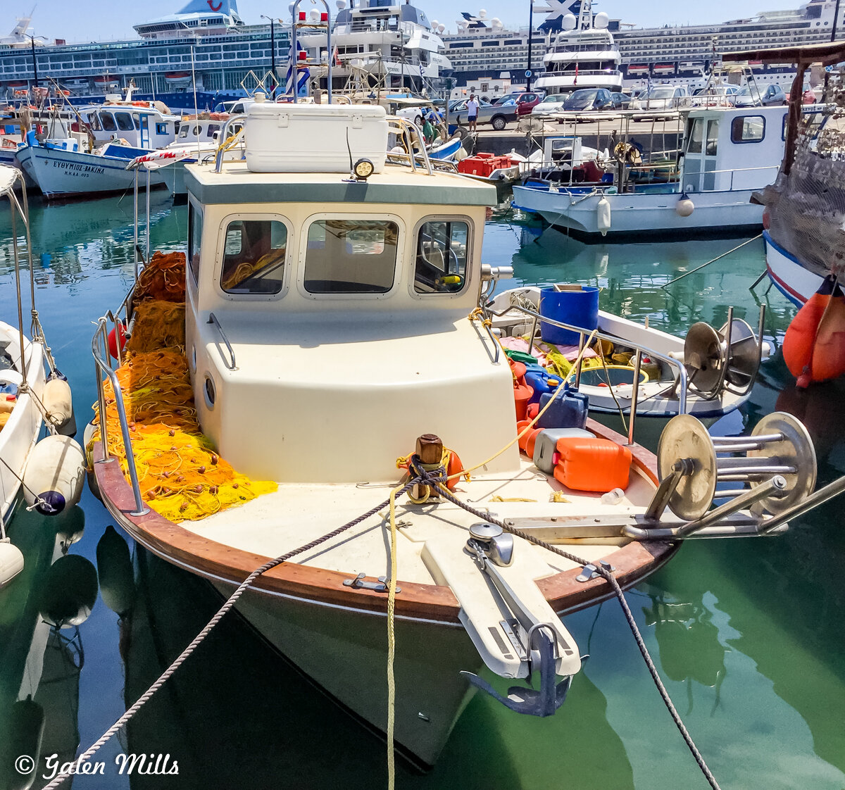 Small fishing boat with nets in a marina filled with various boats and yachts.