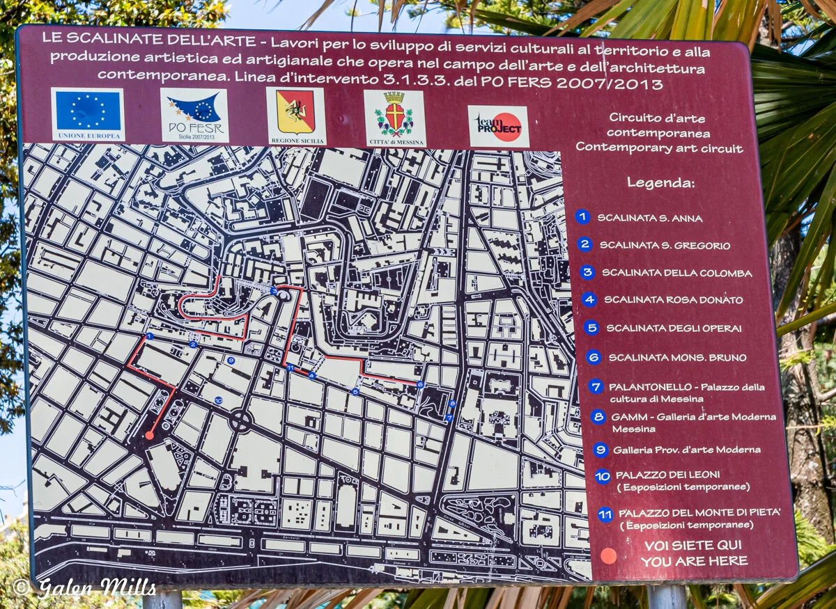 A map sign in Italian showing the contemporary art circuit in Messina, Italy, featuring locations like Scalinata S. Anna, Scalinata S. Gregorio, and various art galleries. A 'You Are Here' marker is present.
