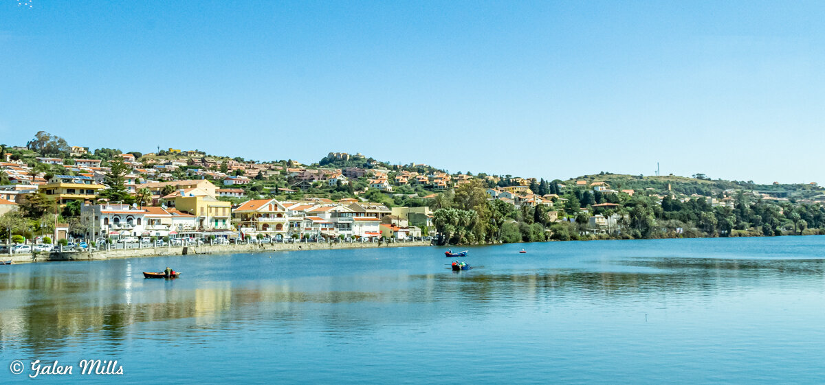 Scenic view of a coastal town with colorful houses, calm water, and small boats on a sunny day.