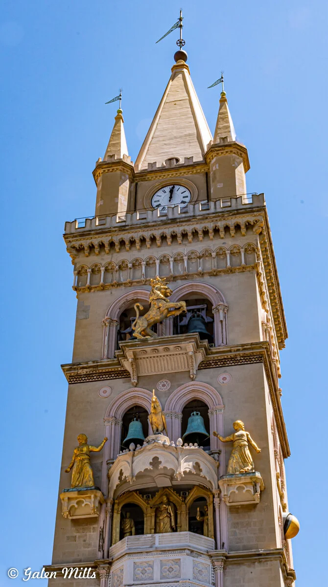 Bell tower with clock and bronze statues against a blue sky