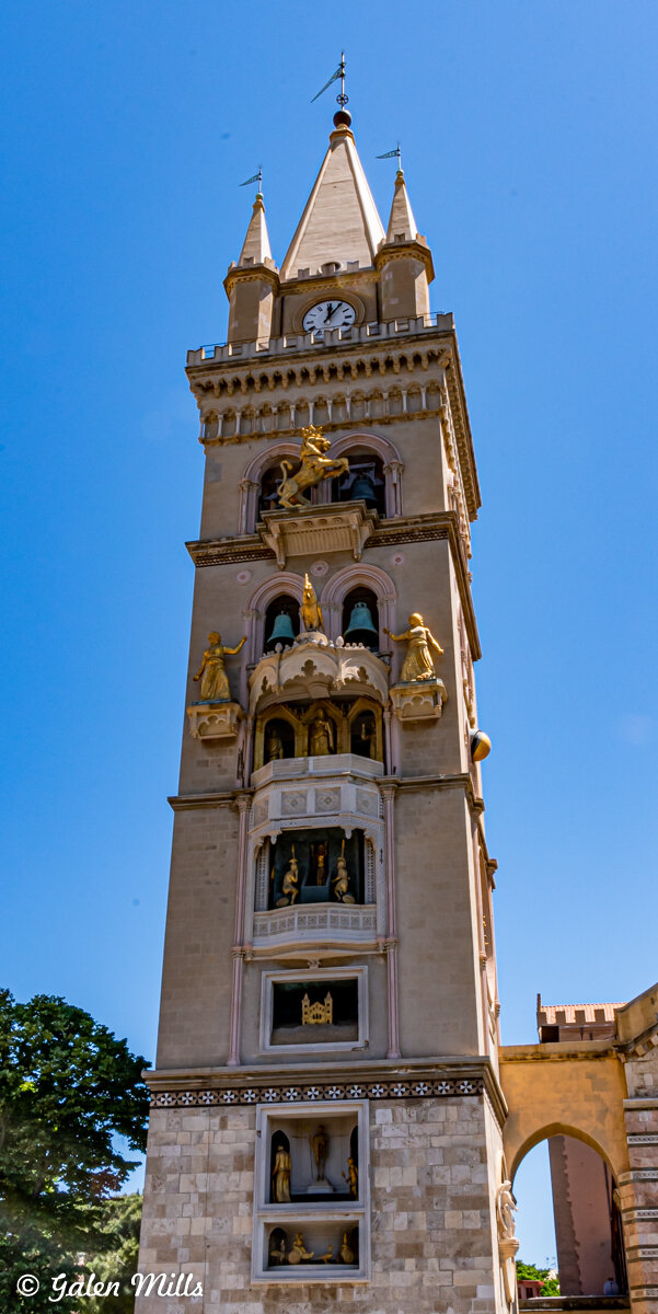 Clock tower with ornate sculptures and a clock face, against a clear blue sky.