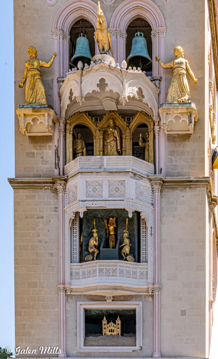 Clock tower detail with statues and bells, featuring gold figures and architectural elements on the facade.