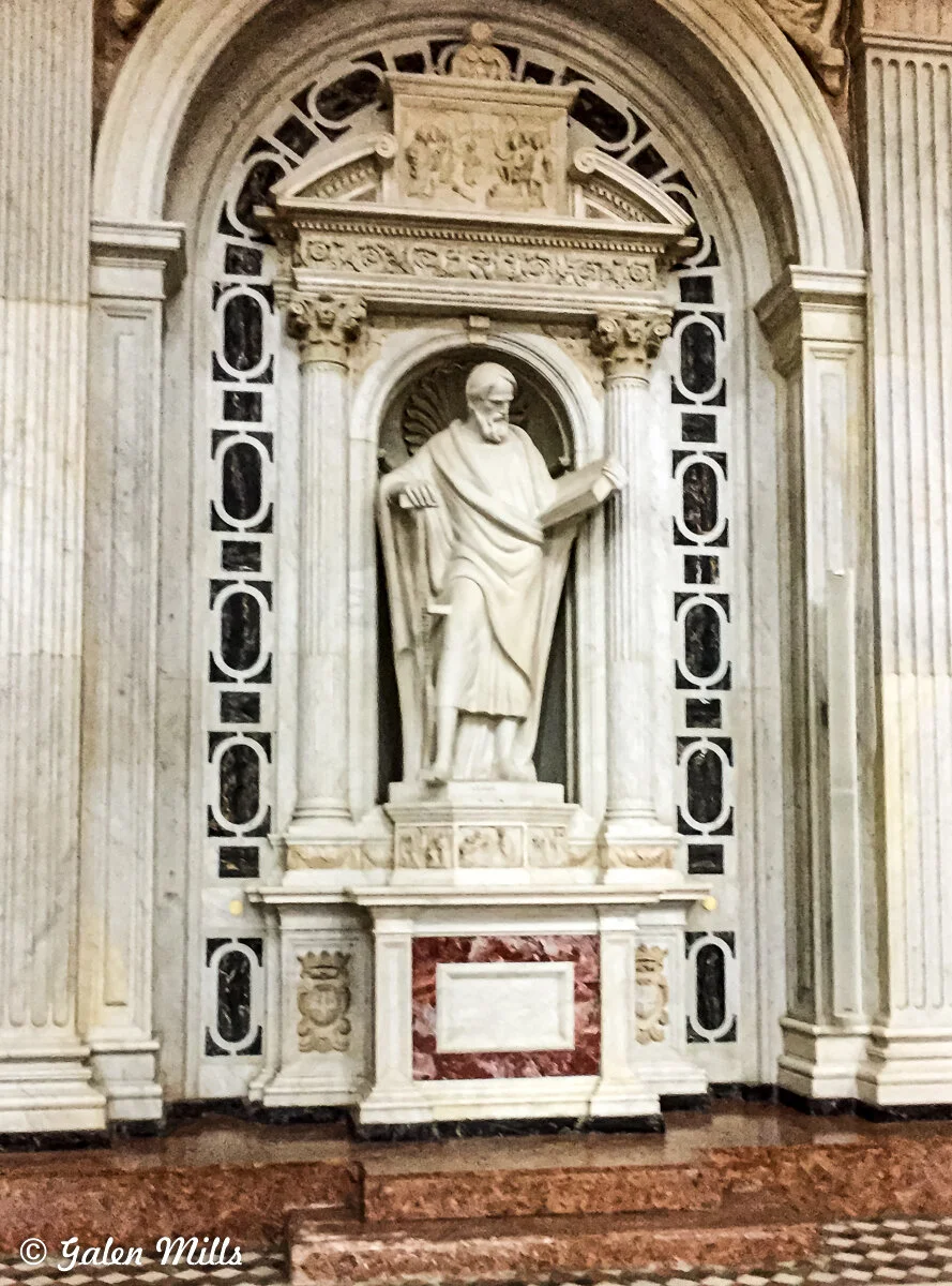Statue of a robed figure in an ornate architectural niche inside a building.