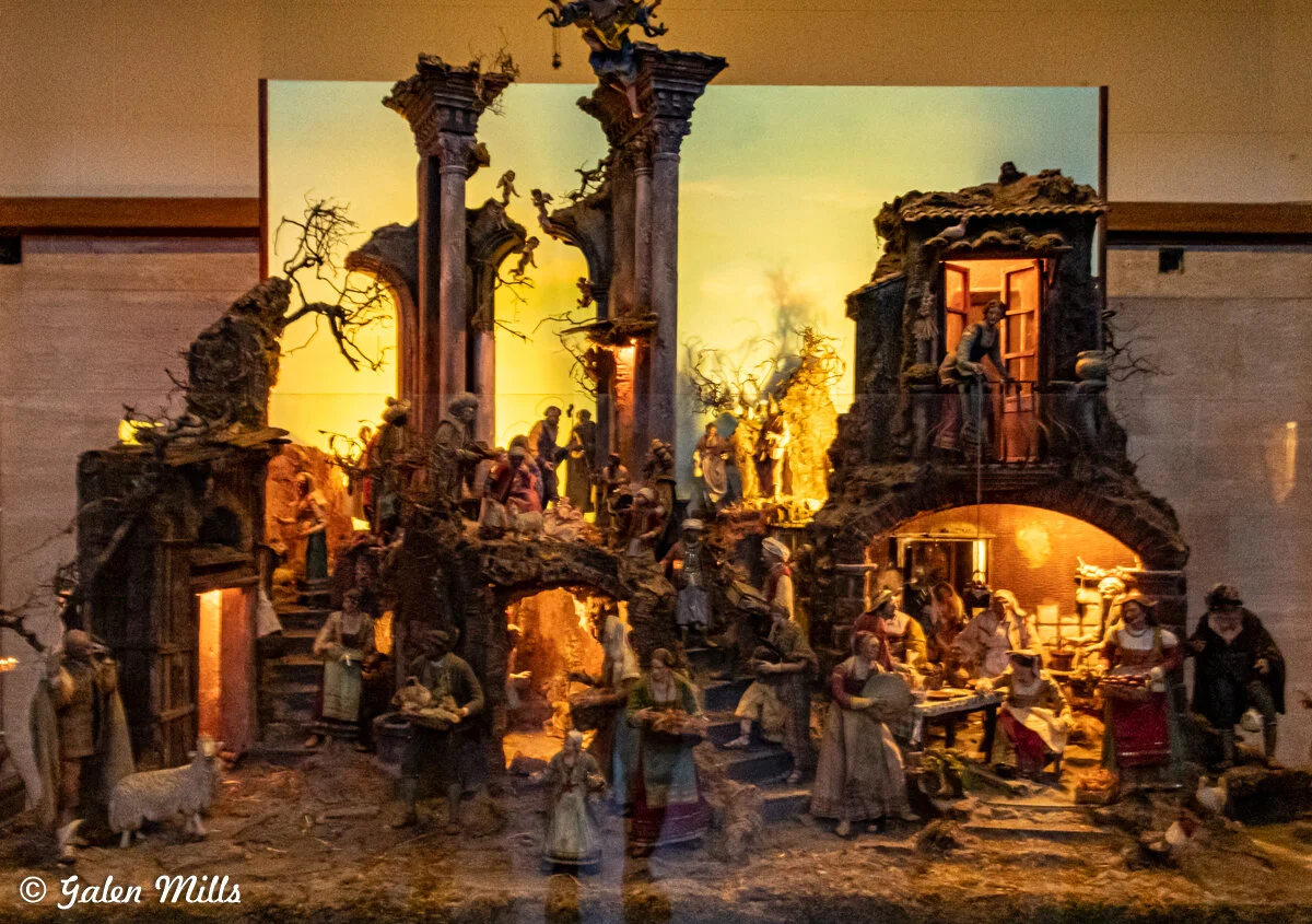 Intricate nativity scene display with numerous figurines depicting biblical characters and animals, set in a detailed architectural backdrop.