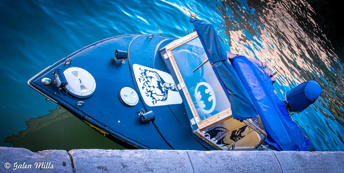 Black boat with Batman logo and illustrations near a dock.